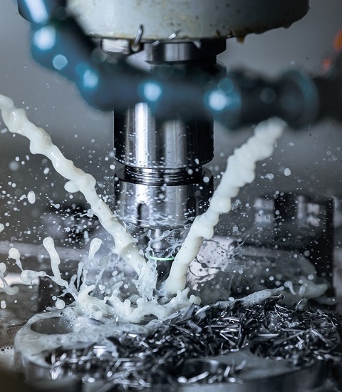 a process of vertical cnc steel milling with external water coolant streams, splashes and a lot of metal chips - close-up with selective focus
